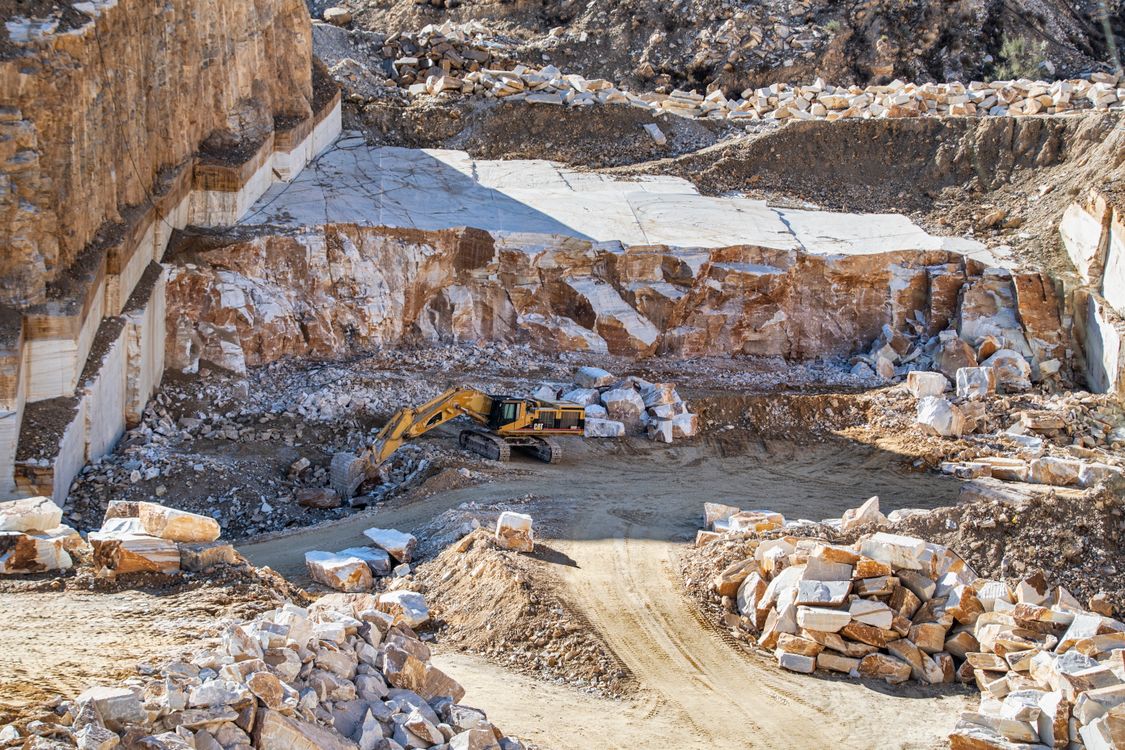 Yellow excavator operating on the floor of a stone quarry