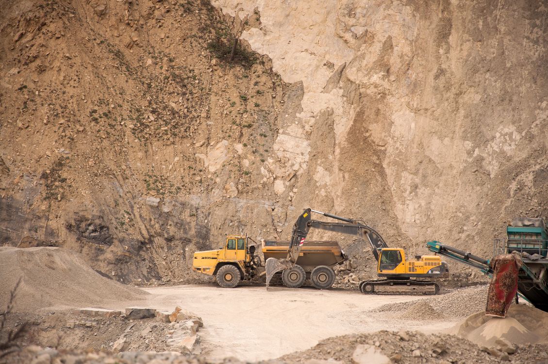 Excavator and articulated dump truck working at a quarry rock face