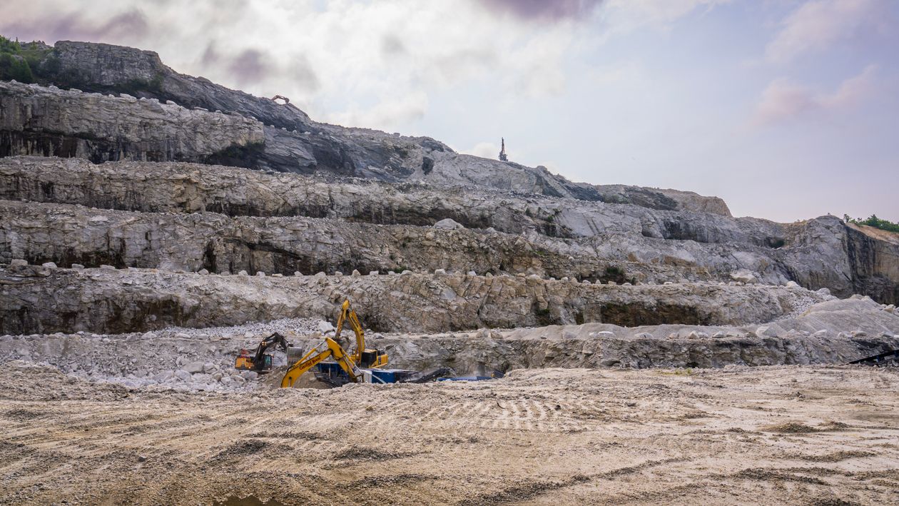 Excavators working beneath terraced rock faces in a quarry